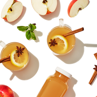 Two citrus beverages styled with red apple slices and some green foliage